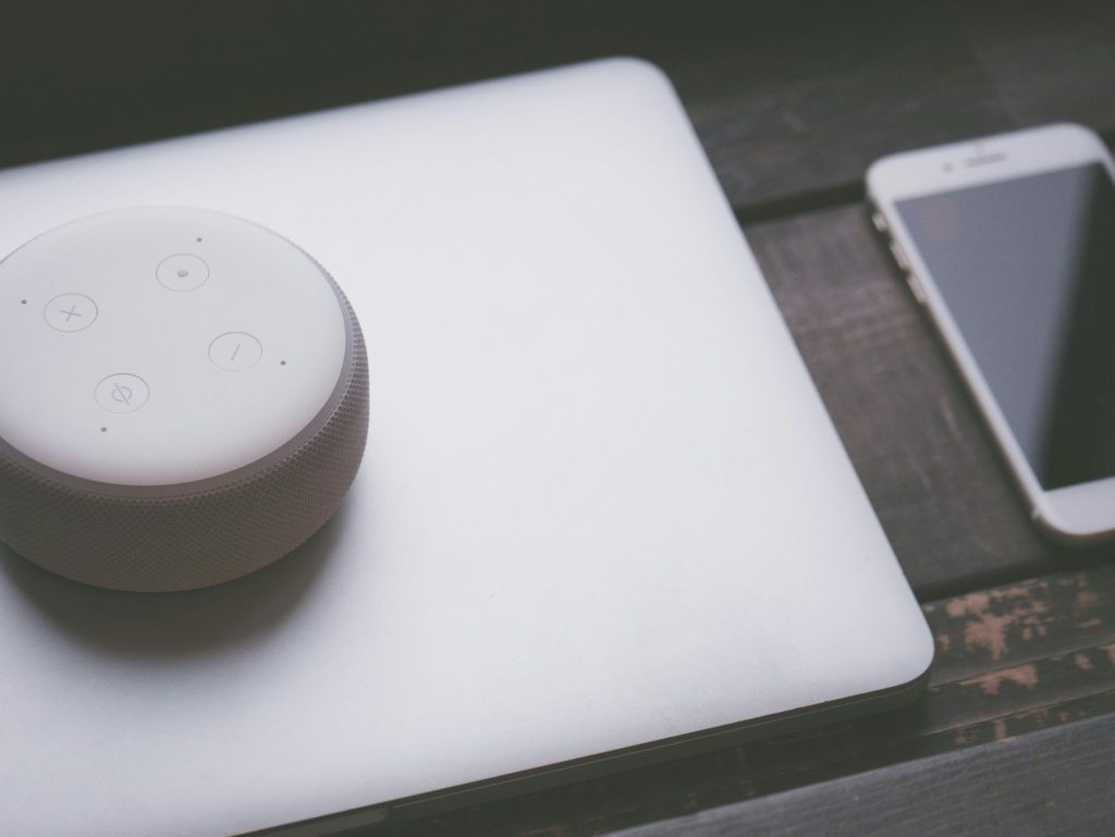 A smart speaker, laptop, and smartphone array representing modern technology lifestyle on a wooden surface.